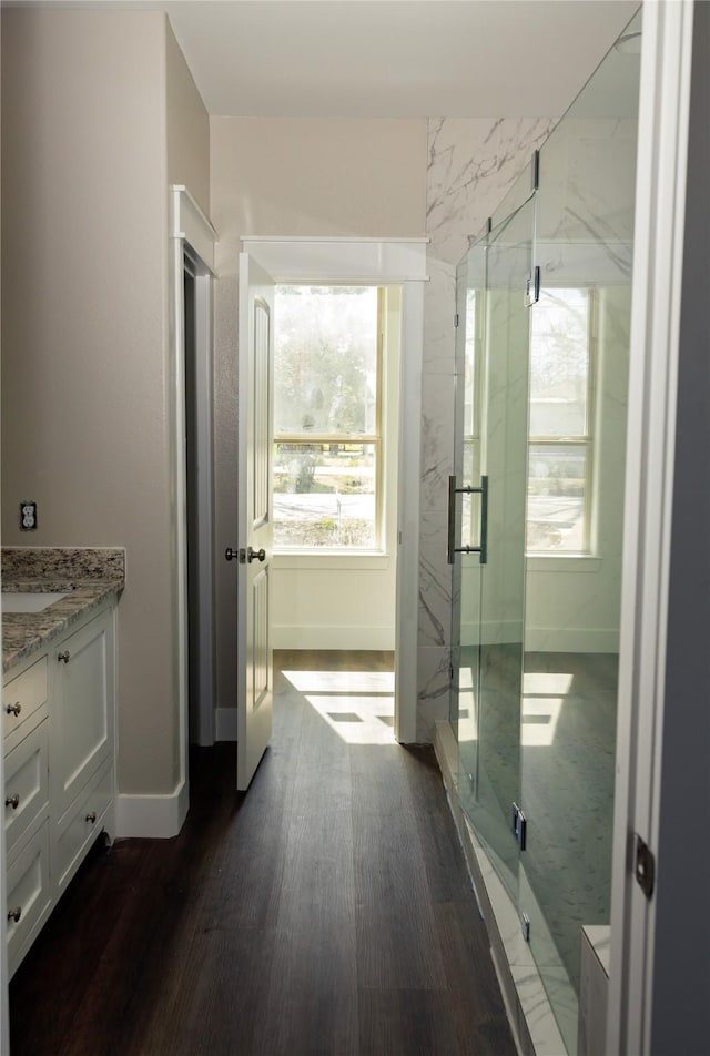 bathroom featuring vanity, wood finished floors, a marble finish shower, and baseboards