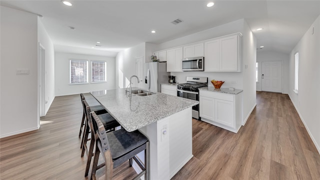 kitchen with appliances with stainless steel finishes, white cabinets, a kitchen island with sink, a sink, and a kitchen bar