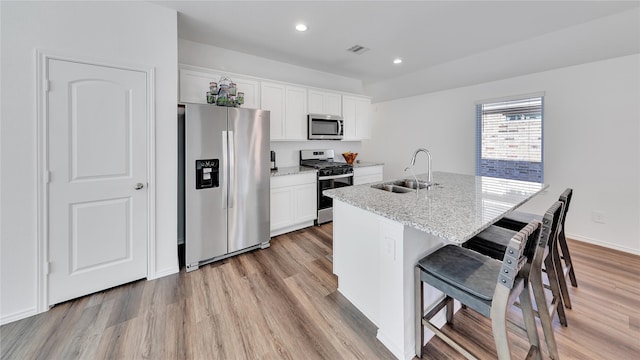 kitchen featuring stainless steel appliances, a sink, visible vents, light wood finished floors, and a center island with sink