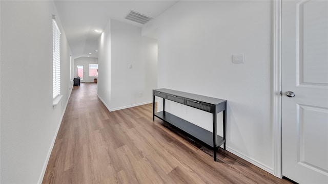 hallway featuring lofted ceiling, light wood-style flooring, visible vents, and baseboards