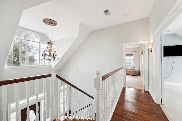 hallway with visible vents, lofted ceiling, wood-type flooring, an upstairs landing, and a notable chandelier