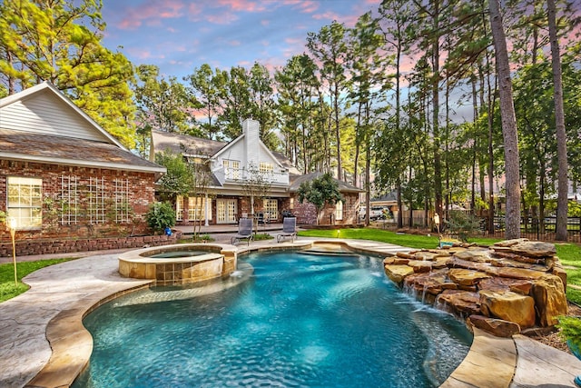 pool at dusk with a pool with connected hot tub, fence, and a patio