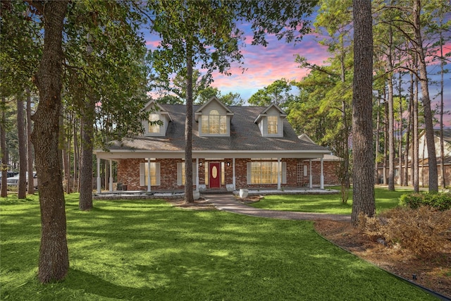 cape cod home featuring a porch, a lawn, and brick siding