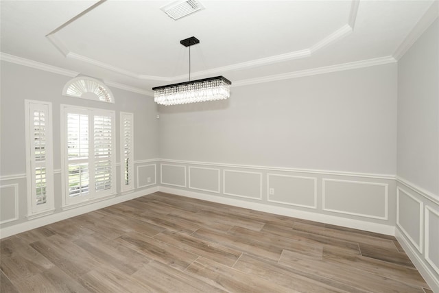 unfurnished dining area with a tray ceiling, a decorative wall, visible vents, and light wood-style floors