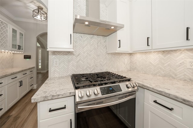 kitchen featuring stainless steel range with gas cooktop, arched walkways, ornamental molding, white cabinets, and wall chimney exhaust hood