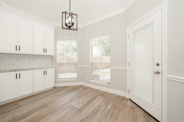 unfurnished dining area featuring light wood-style floors, crown molding, baseboards, and an inviting chandelier