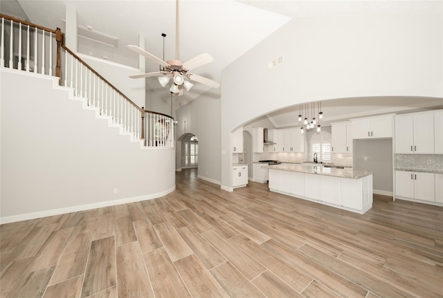 unfurnished living room featuring visible vents, arched walkways, a ceiling fan, light wood-style flooring, and high vaulted ceiling