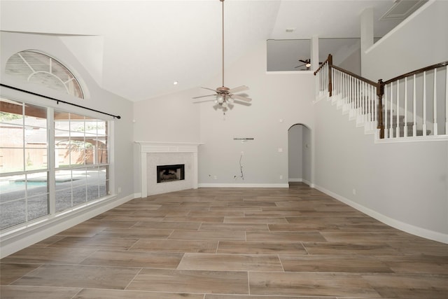 unfurnished living room with arched walkways, a ceiling fan, wood tiled floor, a fireplace, and high vaulted ceiling