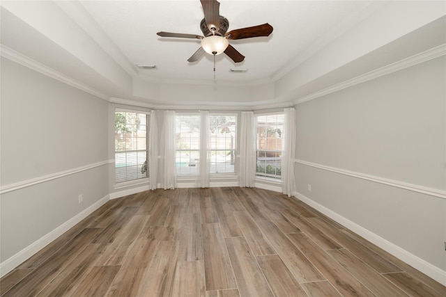 unfurnished room with a tray ceiling, baseboards, visible vents, and light wood finished floors