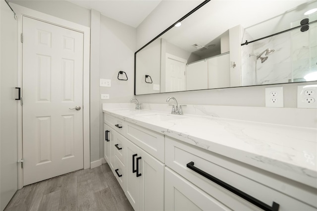 full bath with double vanity, visible vents, a sink, and wood finished floors