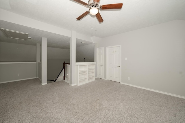 carpeted empty room with lofted ceiling, ceiling fan, attic access, and baseboards