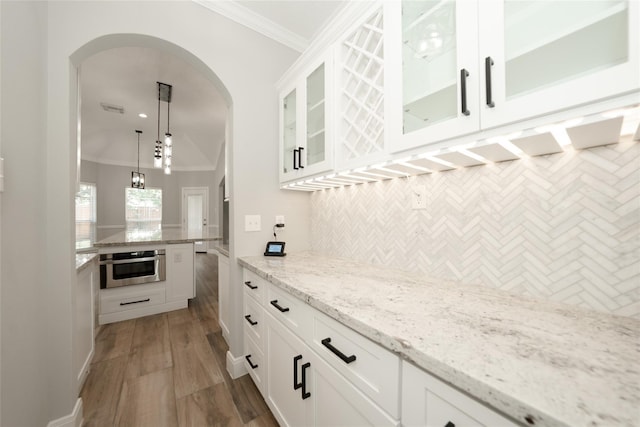 kitchen with arched walkways, decorative backsplash, ornamental molding, stainless steel oven, and wood finished floors