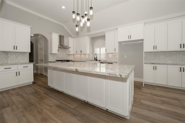 kitchen featuring lofted ceiling, white cabinetry, a sink, wood finished floors, and wall chimney exhaust hood