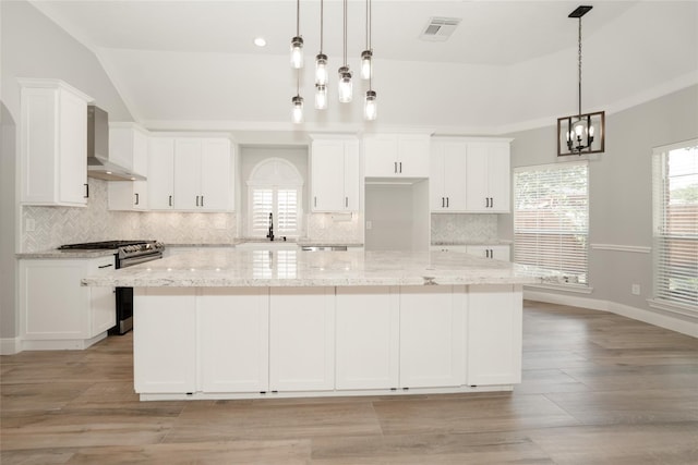 kitchen with a spacious island, wall chimney exhaust hood, white cabinetry, a sink, and gas stove