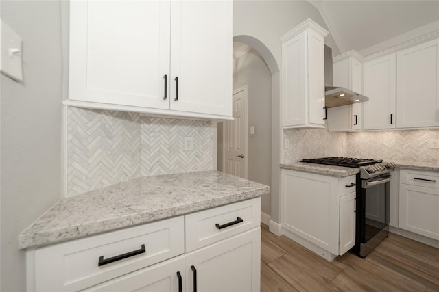 kitchen with light wood finished floors, white cabinets, light stone counters, backsplash, and gas stove