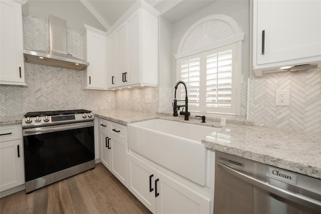 kitchen with stainless steel appliances, a sink, vaulted ceiling, wall chimney range hood, and backsplash