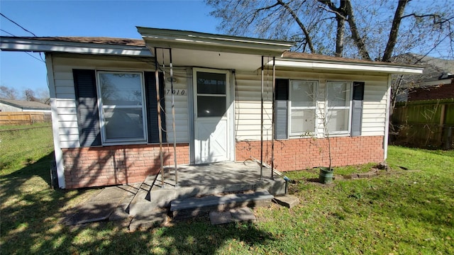 view of exterior entry featuring brick siding, fence, and a lawn