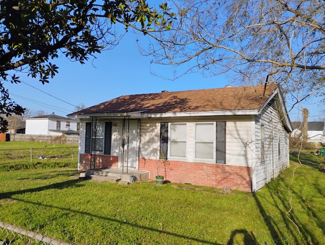 view of front of home featuring brick siding, a front yard, fence, and a shingled roof