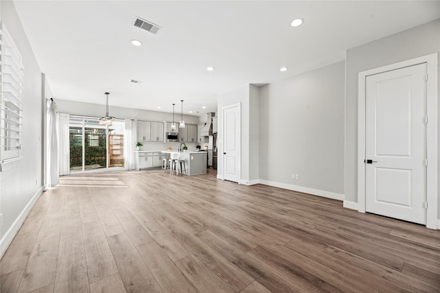 unfurnished living room featuring baseboards, visible vents, wood finished floors, a sink, and recessed lighting