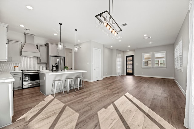 kitchen featuring custom exhaust hood, stainless steel appliances, light countertops, visible vents, and light wood-style flooring