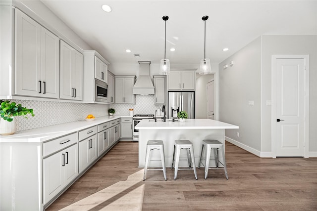 kitchen with custom range hood, stainless steel appliances, light wood-style floors, a kitchen bar, and backsplash