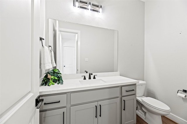 half bathroom with toilet, baseboards, wood finished floors, and vanity