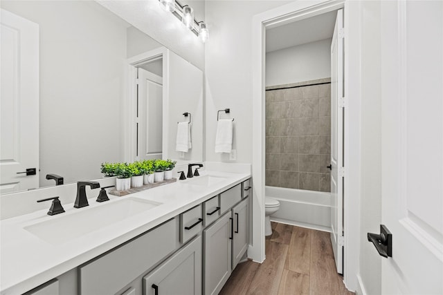 bathroom featuring toilet, double vanity, a sink, and wood finished floors