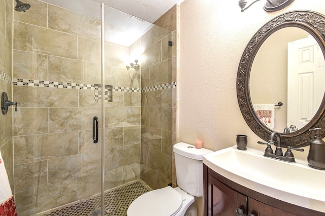 bathroom with a textured wall, a shower stall, toilet, and vanity