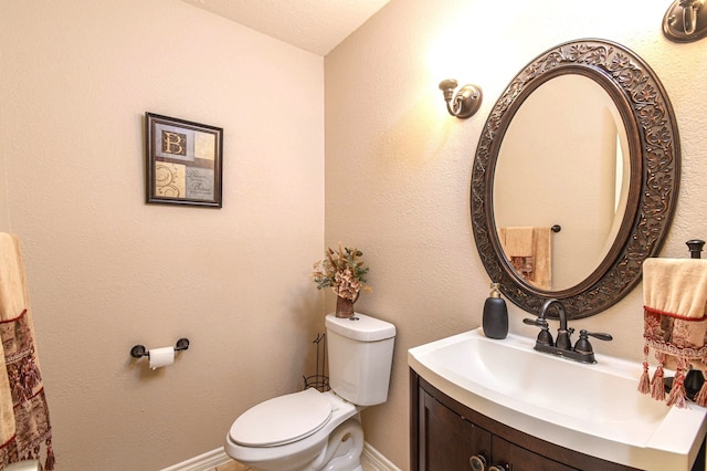 bathroom featuring toilet, a textured wall, baseboards, and vanity