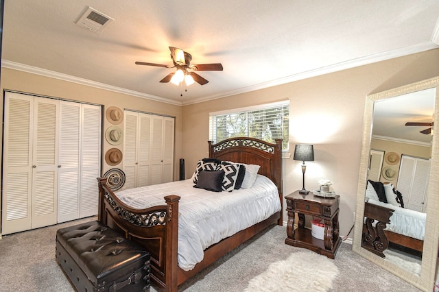 bedroom featuring ornamental molding, visible vents, carpet flooring, and two closets