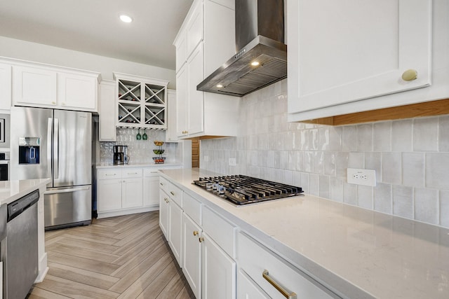 kitchen with wall chimney range hood, tasteful backsplash, appliances with stainless steel finishes, white cabinets, and light countertops