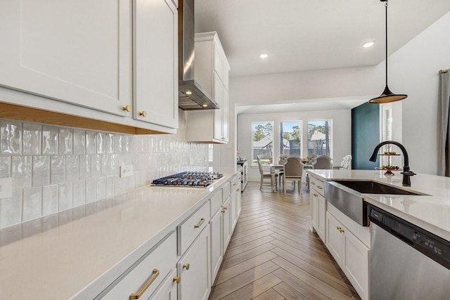 kitchen featuring a sink, stainless steel appliances, light countertops, wall chimney range hood, and tasteful backsplash