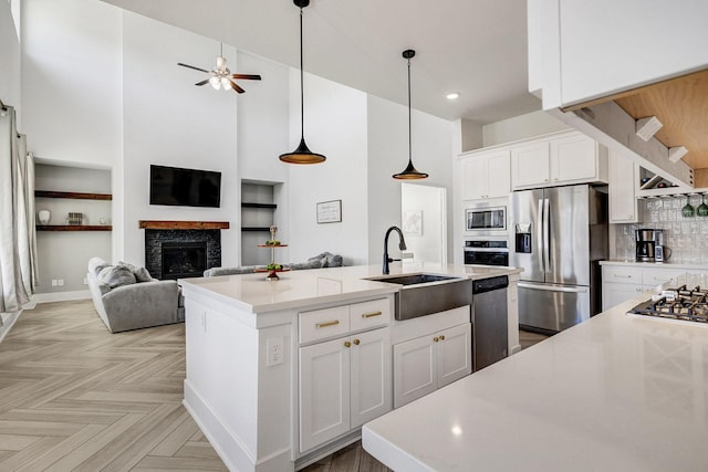 kitchen with a center island with sink, a sink, appliances with stainless steel finishes, a glass covered fireplace, and open floor plan