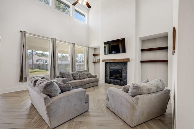 living room with built in shelves, baseboards, a fireplace, a towering ceiling, and a ceiling fan