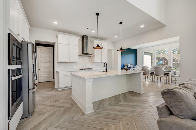 kitchen with a sink, stainless steel appliances, light countertops, wall chimney range hood, and open floor plan