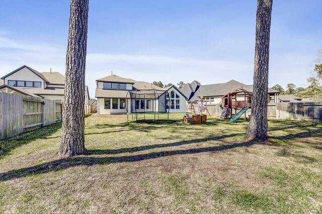 rear view of property featuring a lawn, a trampoline, a fenced backyard, and a playground