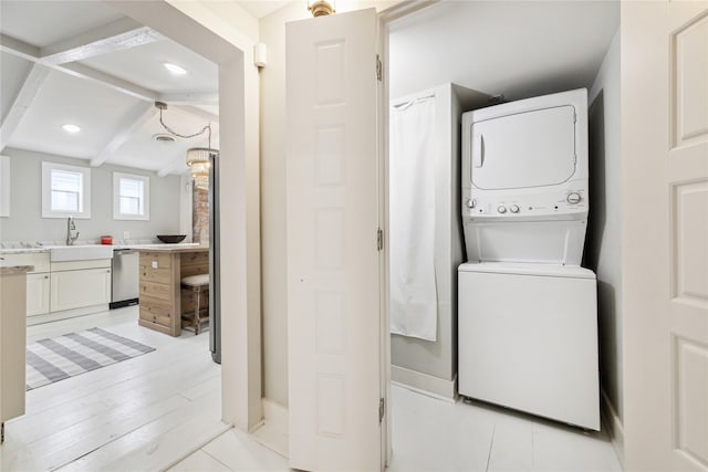 laundry area with light wood finished floors, laundry area, stacked washer and clothes dryer, and a sink