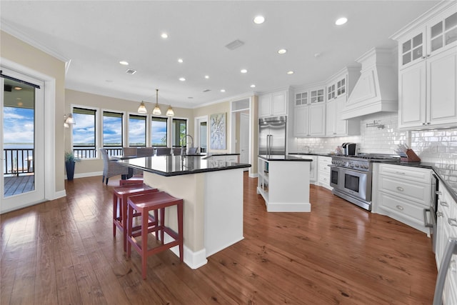 kitchen featuring a kitchen island with sink, premium range hood, visible vents, decorative backsplash, and high end appliances