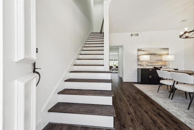 staircase featuring baseboards, wood finished floors, visible vents, and an inviting chandelier