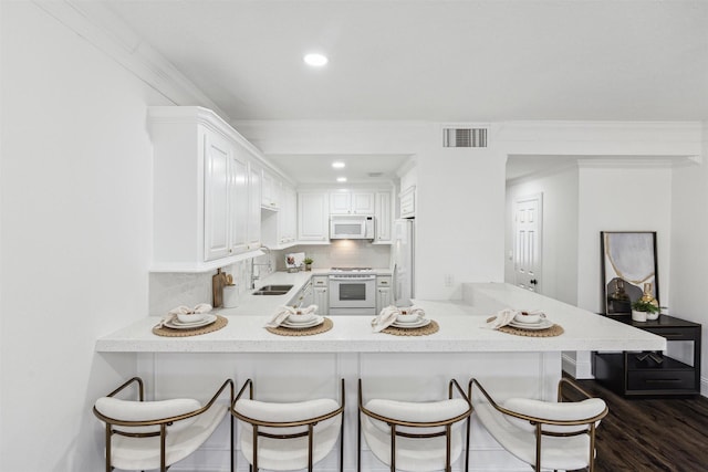 kitchen featuring white appliances, dark wood-style flooring, a peninsula, a sink, and backsplash