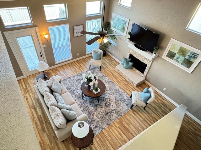living room featuring a wealth of natural light, a stone fireplace, baseboards, and wood finished floors