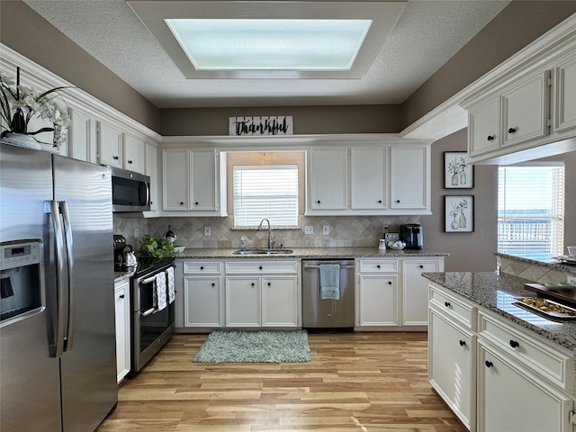 kitchen with light wood-type flooring, white cabinetry, appliances with stainless steel finishes, a sink, and backsplash