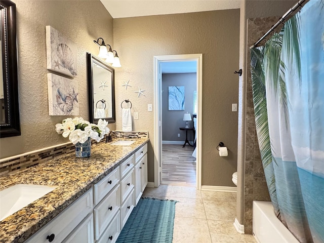 bathroom with a textured wall, tile patterned floors, double vanity, and a sink