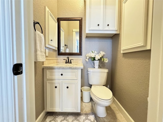 half bath featuring toilet, vanity, a textured wall, and baseboards