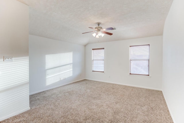 spare room with carpet flooring, vaulted ceiling, a textured ceiling, ceiling fan, and baseboards