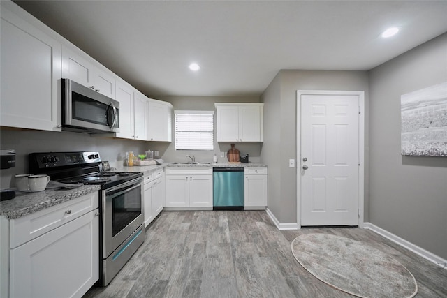 kitchen with a sink, baseboards, white cabinets, appliances with stainless steel finishes, and light wood finished floors