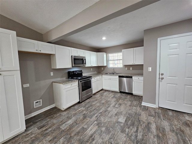 kitchen with appliances with stainless steel finishes, white cabinetry, a sink, and dark wood-style floors