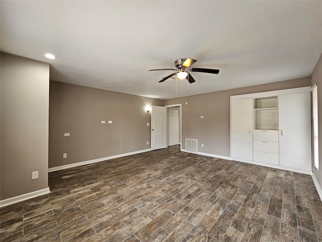 unfurnished bedroom featuring baseboards, visible vents, dark wood finished floors, ceiling fan, and multiple closets