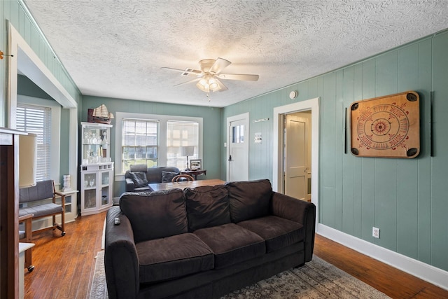 living area with baseboards, a textured ceiling, a ceiling fan, and wood finished floors