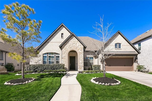 french country inspired facade featuring a garage, a front yard, concrete driveway, and brick siding